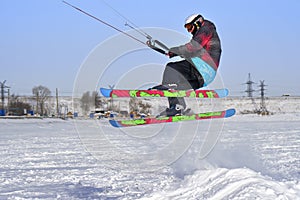 A male athlete engaged in snow kiting on the ice of a large snowy lake. He performs the jump. Winter sunny frosty day.