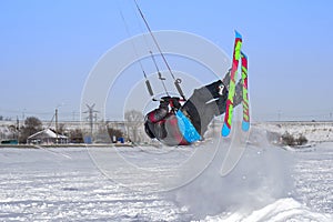 A male athlete engaged in snow kiting on the ice of a large snowy lake. He performs the jump. Winter sunny frosty day.