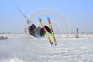 A male athlete engaged in snow kiting on the ice of a large snowy lake. He performs the jump. Winter sunny frosty day