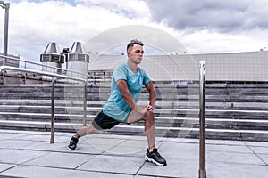 Male athlete guy, in summer in city, doing warm-ups of knees of joints and legs, ankle-boot, before morning jogging
