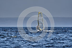 A male athlete is interested in windsurfing. He moves on a Sailboard on a large lak