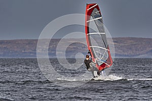 A male athlete is interested in windsurfing. He moves on a Sailboard on a large lake