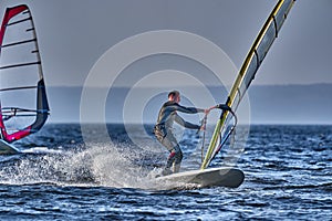 A male athlete is interested in windsurfing. He moves on a Sailboard on a large lake