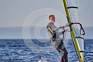 A male athlete is interested in windsurfing. He moves on a Sailboard on a large lake