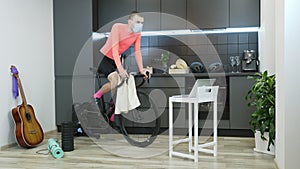 Male athlete in protective medical face mask training on stationary bicycle while watching online cycling trainings at home during