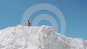 Male athlete runs on a white mountain raising hands up.