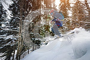 A male athlete skier rides a freeride in a winter forest in the mountains. Jump against the backdrop of snow-covered