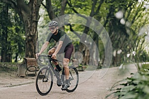 Male athlete in sportswear biking along city park
