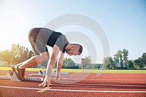 Male athlete on starting position at athletics running track.