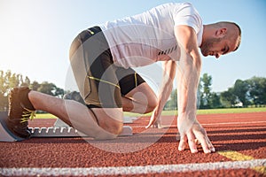 Male athlete on starting position at athletics running track.