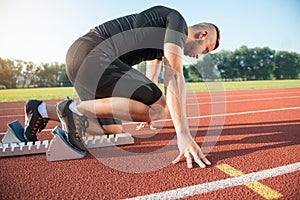 Male athlete on starting position at athletics running track.