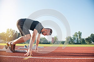 Male athlete on starting position at athletics running track.