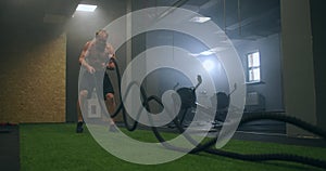 Male athlete working out with ropes in old building. Athlete man in training with ropes near mirror. Battle Rope