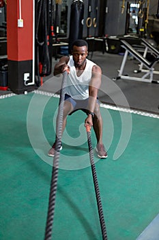 Male athletic exercising with battle ropes in fitness center