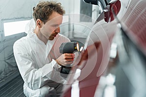 Male auto colorist with lamp matches car color in garage.