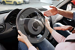 Male auto instructor takes exam in young woman. Cut view of woman`s hands on steering wheel. Guy point on it and explain