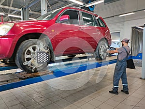 A male auto mechanic repairs a red car raised on a lift in a workshop. The broken car was taken to a car repair shop for