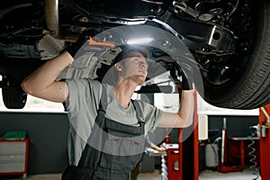 Male auto mechanic working under car lifted on elevator with flashlight