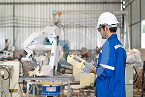 Male automation engineer using remote controller control robot arm welding machine in an industrial factory