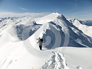 Male back country skier carrying his skis along a narrow snow ridge