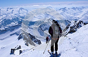 Male backcountry skier skiing down from a high alpine summit with a large backpack and solar panel