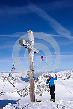 Male backcountry skier at the summit cross of a high alpine peak on a beautiful winter day