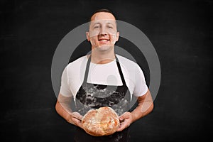 Male baker in an apron with bread in his hands on a black background