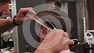 A male Barber cuts the hair on the client`s head using scissors and a comb.