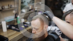 Male barber with a male client at barbershop. Barber cutting hair with scissors.