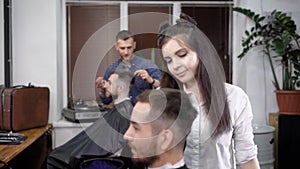 Male barber working with client covered with cutting cape shaping perfectly his haircut with comb and scissors. Female