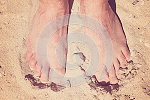 Male bare feet in a warm sand on a sunny beach during vacation.