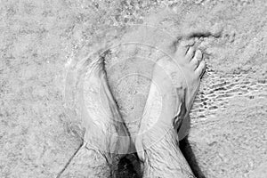 Male bare feet in a warm sand on a sunny beach during vacation.