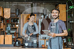 male barista in apron standing holding the digital tablet
