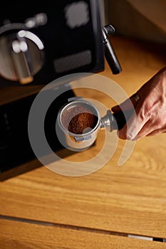 Male barista hand making espresso from ground coffee maker at modern cafe