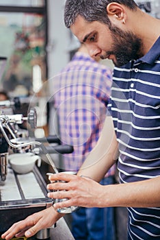 Male barista making cappuccino at counter in coffeeshop