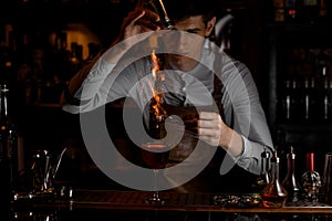 Male bartender add spices for a decor in the fire above a delicious red cocktail in the glass