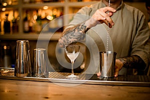Male bartender holding long bar spoon and stirring cocktail in mixing cup