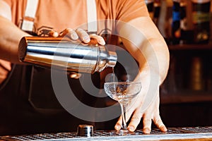 Male bartender is making cocktail pouring alchohol
