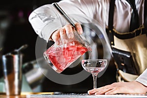 Male bartender is making cocktail pouring alchohol from jug to g photo