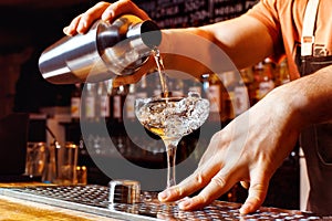 Male bartender is making cocktail pouring alchohol from shaker photo