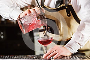 Male bartender is making cocktail pouring alcohol from jug to glass