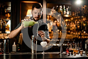 Male bartender pouring a pistachio color liqour from the glass bottle to the steel jigger photo