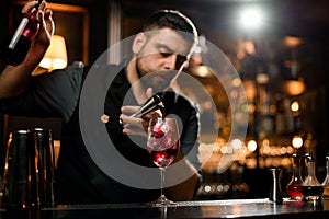 Male bartender pouring a red liqour from the jigger to a cocktail glass holding a bottle photo