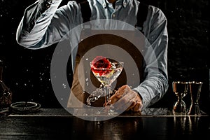 Male bartender throwing a big red rose bud to a martini glass with a alcoholic cocktail