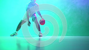 Male basketball player in motion, training, coordinating ball in dribbling technique on gradient green, cyan background