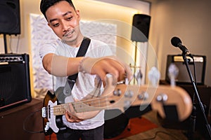 a male bassist tunes an electric guitar bass string before playing