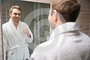 Male in bathrobe looking at himself in bathroom mirror
