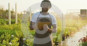 male bearded African american greenhouse worker with clipboard inspects plants