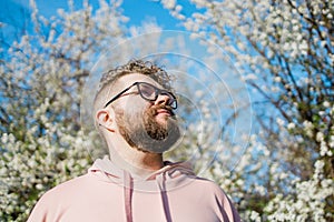 Male bearded man standing under branches with flowers of blooming almond or cherry tree in spring garden. Spring blossom