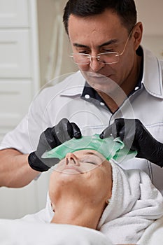 male beautician removing green alginate mask from face of woman